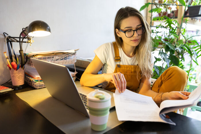 Millennial,Woman,Gardener,In,Yellow,Overalls,Using,Laptop,,Examines,Project