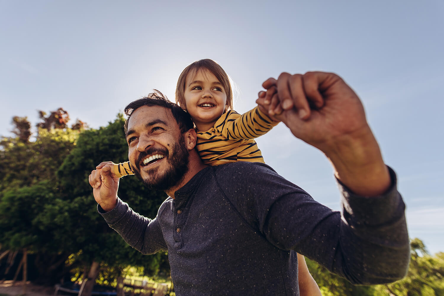Smiling father carrying his young daughter on his shoulders outdoors.