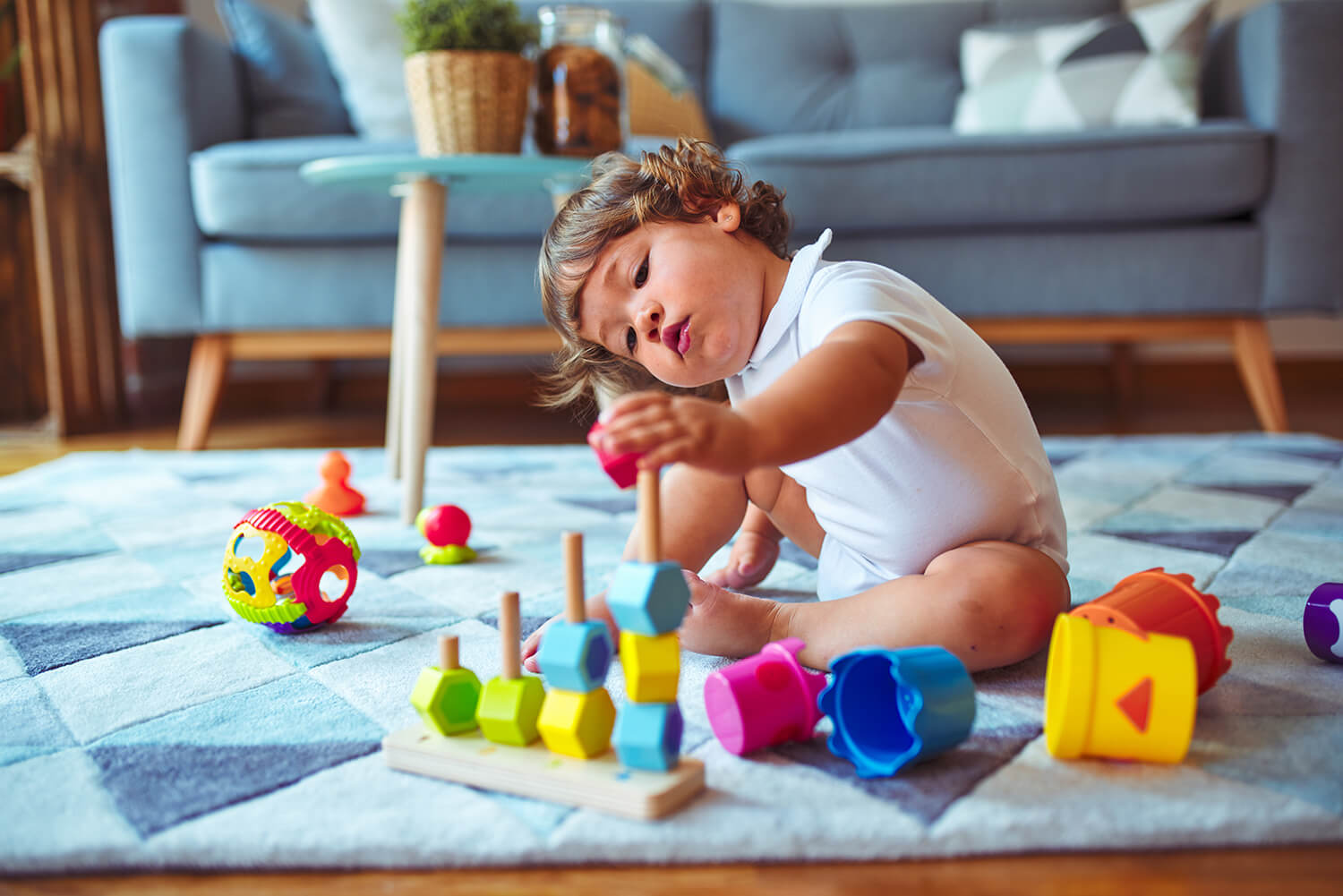 Toddler playing with colourful educational toys on a rug at home.