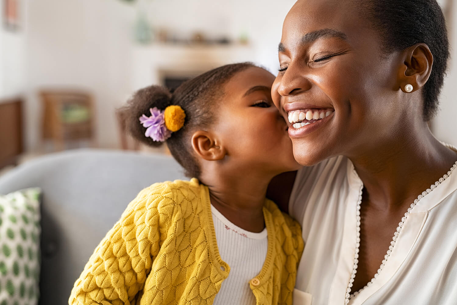 Young girl kissing her smiling mother on the cheek in a cosy family home in Sale, Manchester.