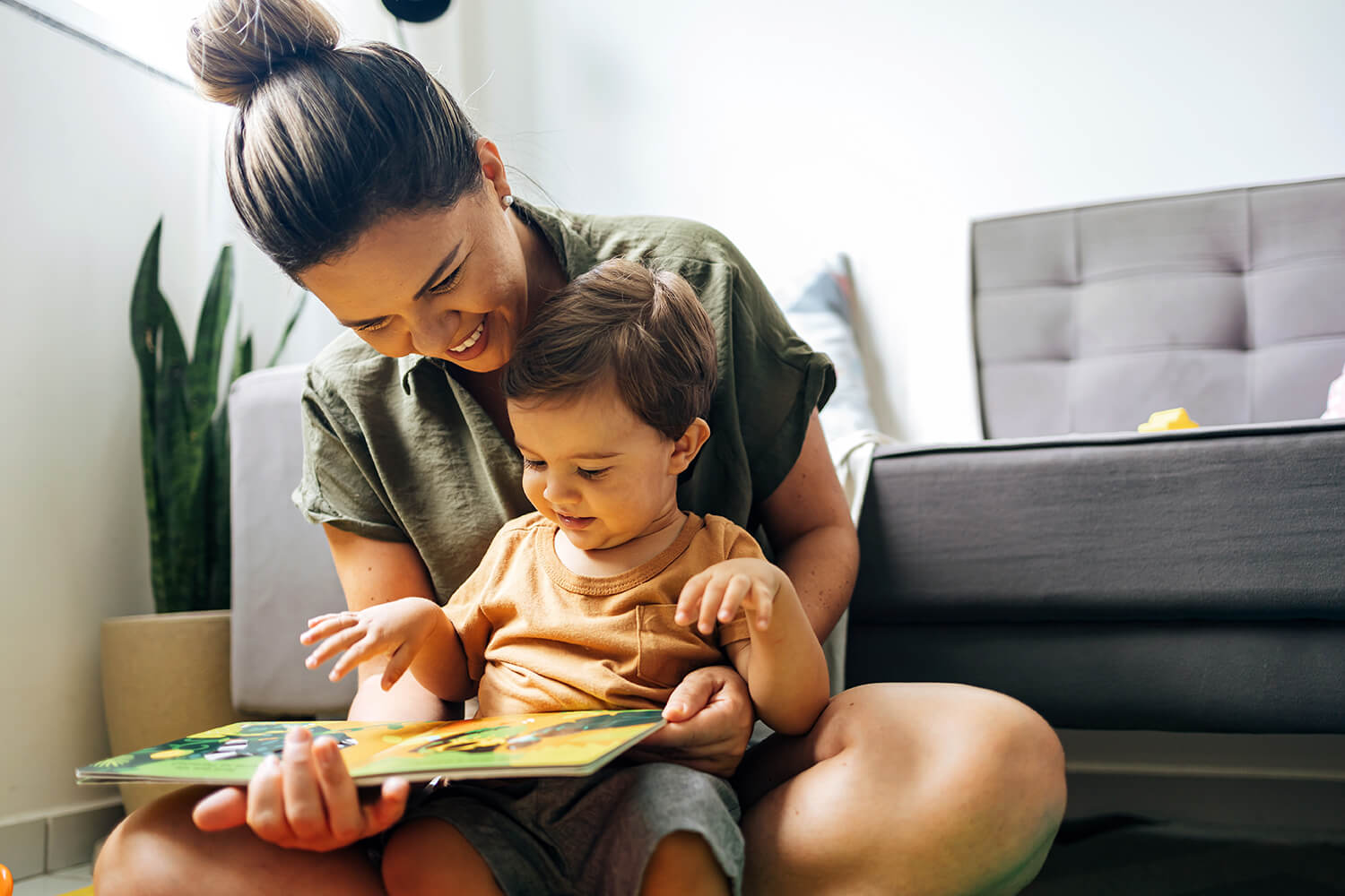 Smiling mother reading a picture book to her toddler in a bright, modern family home.